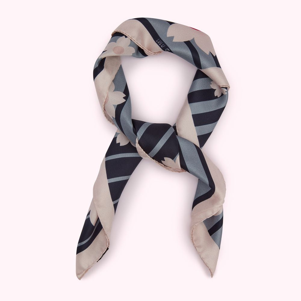 A beige and navy blue silk scarf with a floral pattern, knotted and displayed against a white background.
