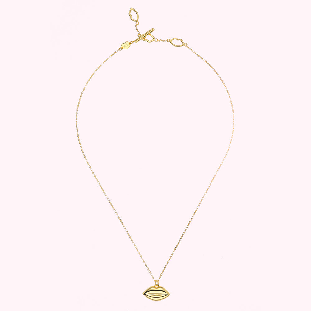 Gold necklace with a lip-shaped pendant against a white background.
