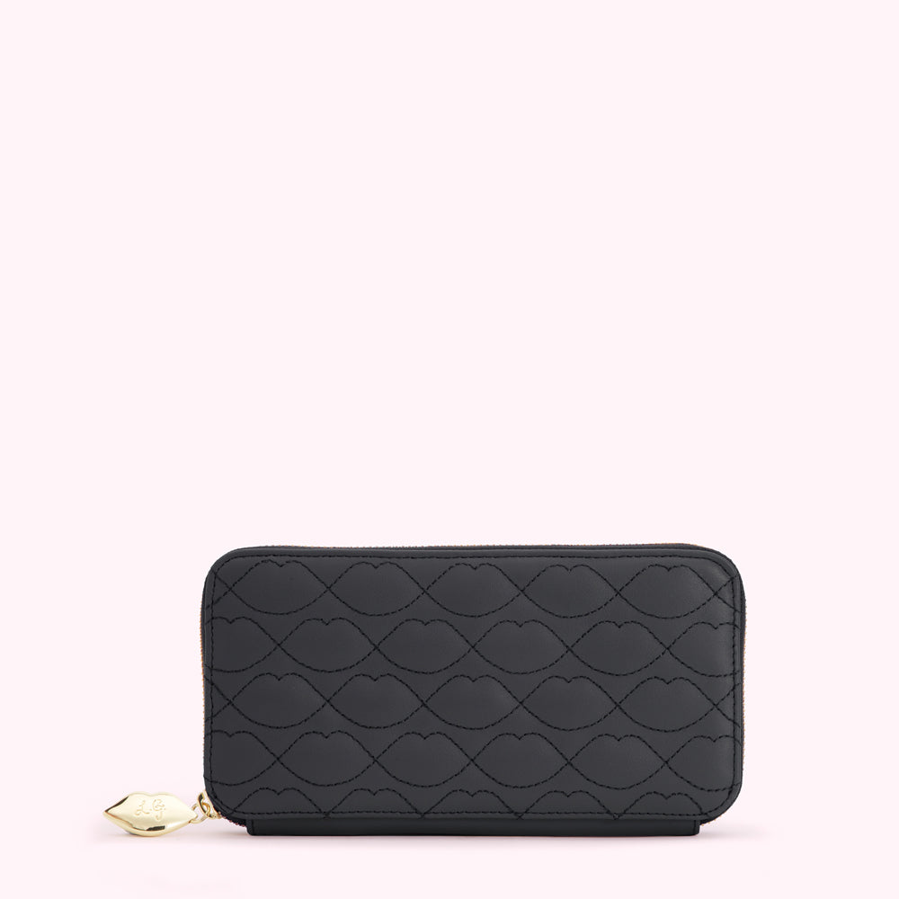 Black quilted zip-around wallet with a lip print pattern on a light pink background.
