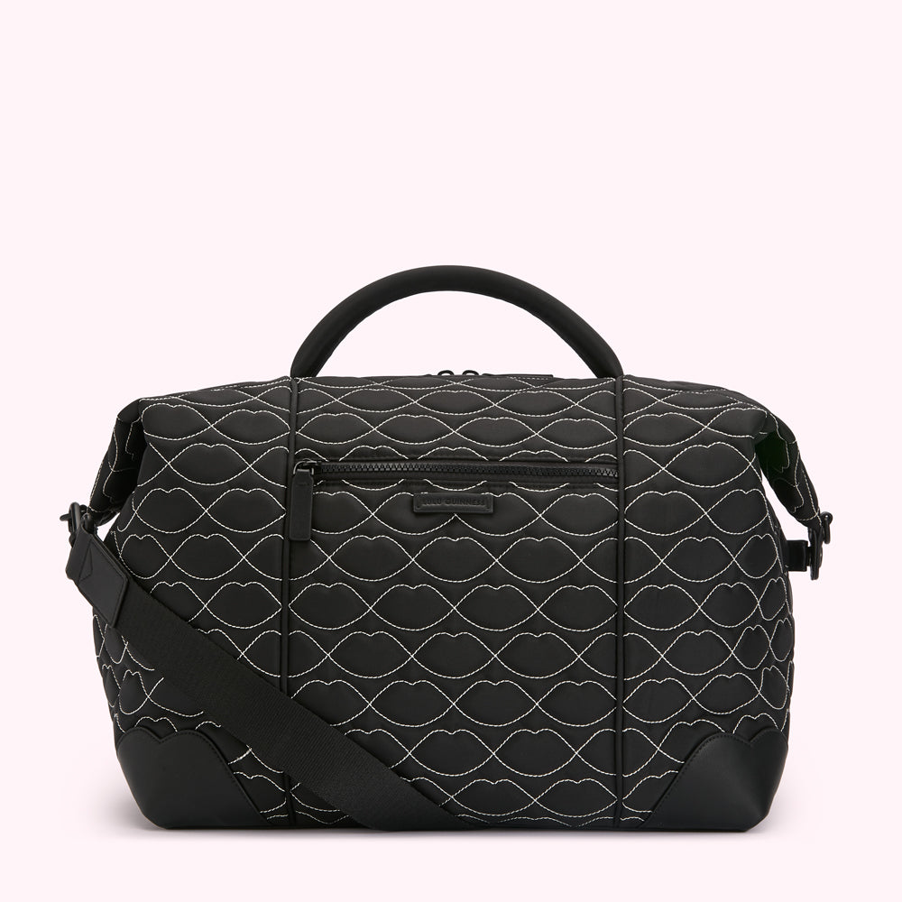 Black quilted bag with a lip print and a long shoulder strap.